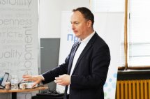 Чоловік у чорному піджаку стоїть у приміщенні.