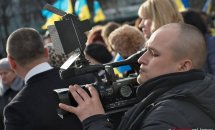 Чоловік тримає відеокамеру в руках. На фоні багато людей.