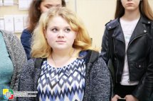 Дівчина зі світлим волоссям дивиться убік. На задньому фоні стоять інші студентки.