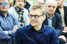 Чоловік в окулярах та синьому одязі дивиться убік.