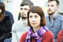 Жінка з темним волоссям та в червоному одязі перебуває у приміщенні.