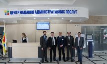 П'ятеро чоловіків у ділових костюмах стоять перед реєстраційною стійкою у приміщенні ЦНАПу.