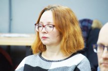 Жінка в окулярах сидить в приміщенні.