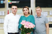 Двоє чоловіків та жінка з букетом троянд позують для фото.