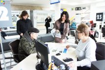 Працівниця консультує чоловіка за робочим місцем. Біля них стоять ще дві жінки.