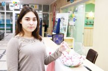 Дівчина дістає щось зі скляної ємності та дивиться у камеру.