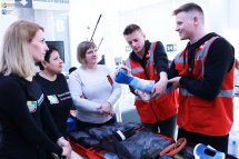 Двоє хлопців у червоних жилетах щось розповідають та показують для трьох жінок.