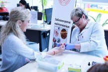 Жінка у білому халаті бере кров з пальця у іншої жінки.