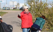 Жінка у червоній куртці прибирає на дворі.