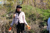 Жінка у світлій куртці прибирає у парку.