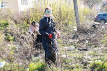 Жінка у темному одязі збирає сміття у чорний пакет у парку.