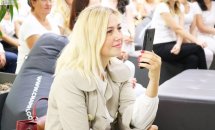 Жінка зі світлим волоссям сидить у приміщенні та тримає телефон у руках.