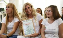 Жінка зі світлим волосся тримає подяку у руках, біля неї ще дві жінки.