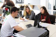Чоловік сидить за робочим столом, а навпроти нього сидить дві жінки.