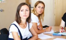 Дві жінки сидять за столом та дивляться убік.