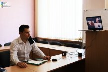 Чоловік у білій сорочці сидить за столом біля нього стоїть ноутбук.