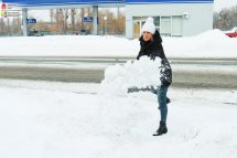 Жінка лопатою кидає сніг.