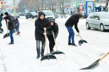 Люди у верхньому одязі прибирають сніг на вулиці.