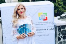 Блондинка з довгим волоссям тримає роздаткові матеріали і усміхається.