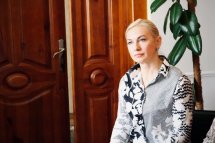 Жінка сидить біля рослини, дивиться вбік.