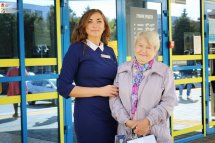 Співробітниця в синьому костюмі спілкується з жінкою похилого віку.