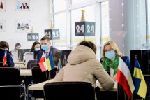  Жінка в бежевому пальті веде розмову з іншою жінкою.