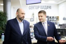Чоловік у костюмі розмовляє з іншим чоловіком у приміщенні.
