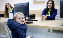 Дитина сидить за столом біля адміністраторів, усміхається.