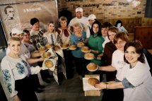 Група людей у традиційному вбранні тримають хліб у руках та усміхаються на камеру.