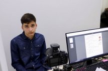 Хлопець сидить перед комп’ютером, поруч стоїть фотоапарат.