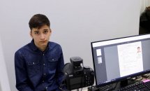Хлопець сидить перед комп’ютером, поруч стоїть фотоапарат.