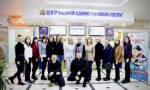 Група людей стоїть у приміщенні перед банером із написом.