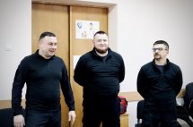 Троє чоловіків у темному одязі стоять разом.