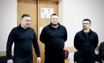 Троє чоловіків у темному одязі стоять разом.