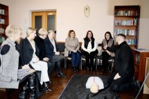 Група людей сидить у класі, на підлозі манекен.