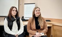 Дві молоді жінки сидять і усміхаються.