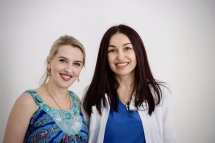 Дві жінки усміхаються, позуючи перед камерою.