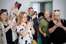 Група людей посміхаються та фотографують на телефон.