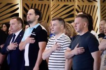 Група людей стоїть у приміщенні з дерев’яним інтер’єром, поклавши руки на серце.