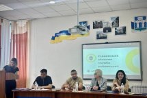 Загальний вигляд конференц-залу, кілька людей за столом, на екрані – презентація.