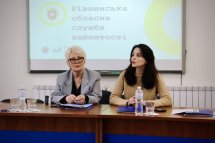 Дві жінки сидять за столом, перед ними мікрофони та вода, на екрані позаду – слайд із текстом.