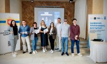 Група людей стоїть у приміщенні на фоні банерів з логотипами.