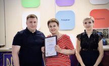 Чоловік у чорній футболці разом із двома жінками позують з сертифікатом.