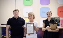 Чоловік у чорній футболці разом із двома жінками фотографуються з сертифікатом.