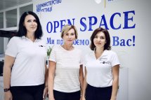 Три жінки у білих сорочках стоять перед стендом із написом "OPEN SPACE".