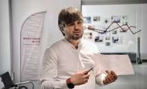 Чоловік із бородою проводить презентацію, тримаючи документ.