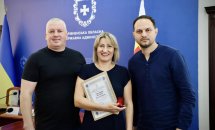 Два чоловіка і жінка з сертифікатом позують на синьому фоні.
