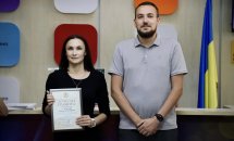 Чоловік та жінка з сертифікатом на фоні прапора.