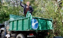 Людина стоїть на вантажівці, завантажуючи мішки зі сміттям.