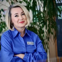 Жінка у синій сорочці з бейджем радісно посміхається.